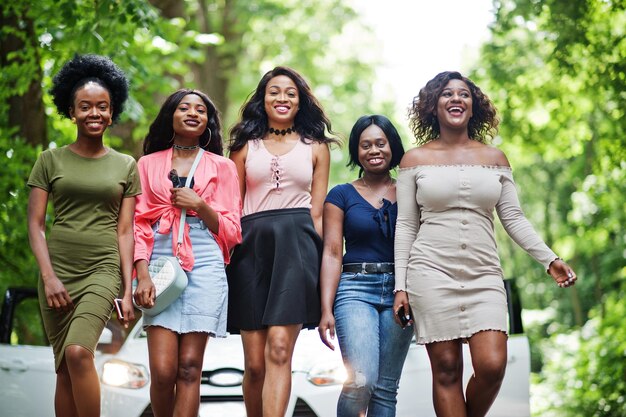Gruppe von fünf glücklichen Afroamerikanern, die gegen ein weißes Auto gehen
