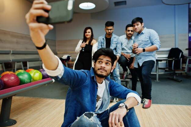 Gruppe von fünf südasiatischen Völkern, die sich im Bowlingclub ausruhen und Spaß haben, Selfie per Telefon machen und kalte Sodagetränke aus Glasflaschen halten