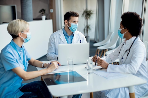 Gruppe von Gesundheitsexperten mit Gesichtsmasken, die sich während eines Treffens in einer medizinischen Klinik unterhalten