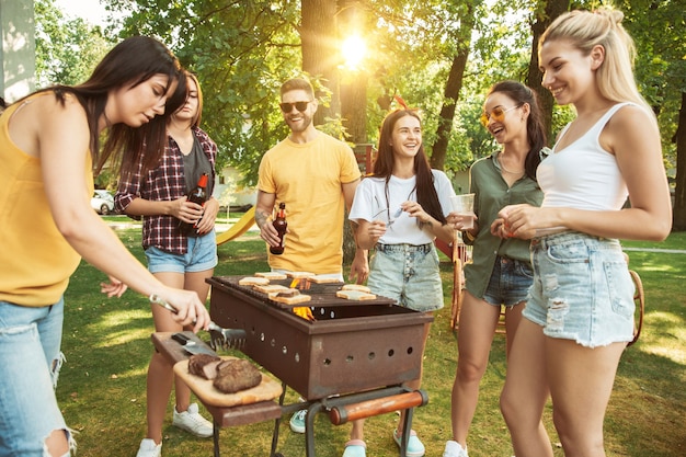 Kostenloses Foto gruppe von glücklichen freunden, die bier und grillparty am sonnigen tag haben. zusammen im freien in einer waldlichtung oder im hinterhof ausruhen