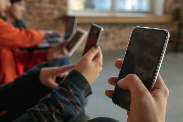 Gruppe von glücklichen jungen jungen Leuten, die zusammen auf einem Sofa sitzen. Teilen Sie Nachrichten, Fotos oder Videos von Smartphones, lesen Sie Artikel oder spielen Sie Spiele und haben Sie Spaß. Social Media, moderne Technologien.