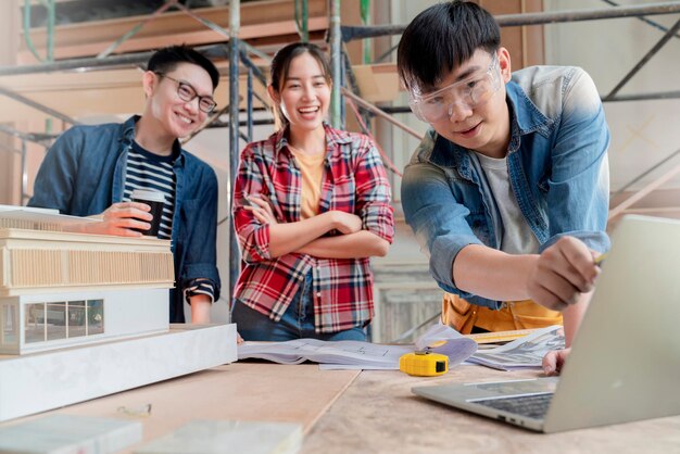 Gruppe von Innenarchitekturteams intelligenter asiatischer Architekten, die sich mit Bauingenieuren beraten, Brainstrom-Treffen mit Hausprojektplan und Hausmodell im Hintergrund der Hausrenovierungsstruktur