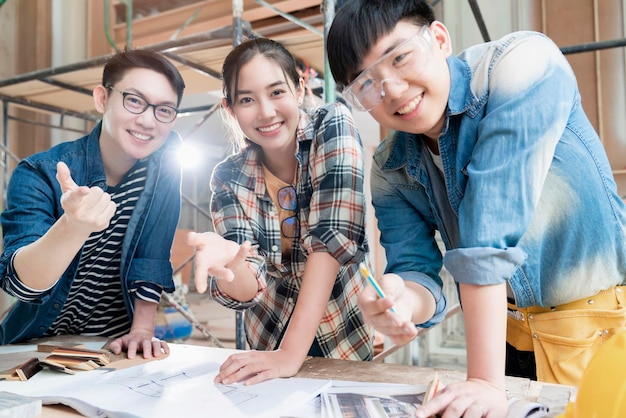Gruppe von Innenarchitekturteams intelligenter asiatischer Architekten, die sich mit Bauingenieuren beraten, Brainstrom-Treffen mit Hausprojektplan und Hausmodell im Hintergrund der Hausrenovierungsstruktur
