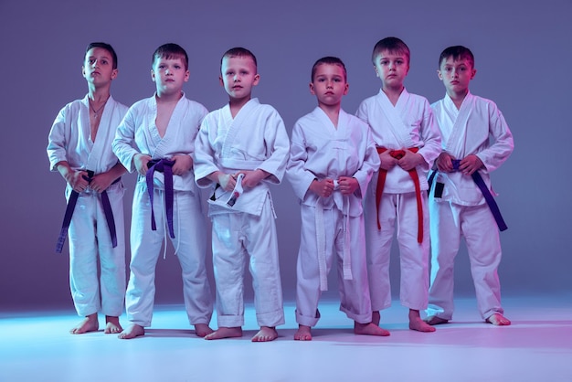 Gruppe von jungen kindern, die kampfkunstkarate trainieren, isoliert über violettem studiohintergrund in neon