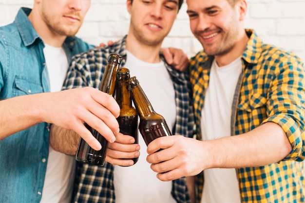 Gruppe von lächelnden drei männlichen Freunden, welche die Bierflasche klirren