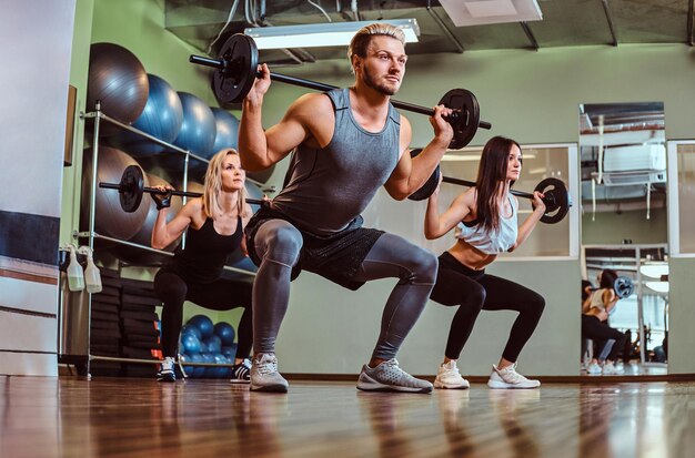 Gruppe von Menschen, die mit der Langhantel trainieren und im Fitnessclub Kniebeugen machen.