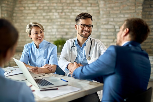 Gruppe von Mitarbeitern des Gesundheitswesens, die einen Finanzberater während des Treffens im Büro begrüßen. Der Fokus liegt auf dem jungen Arzt