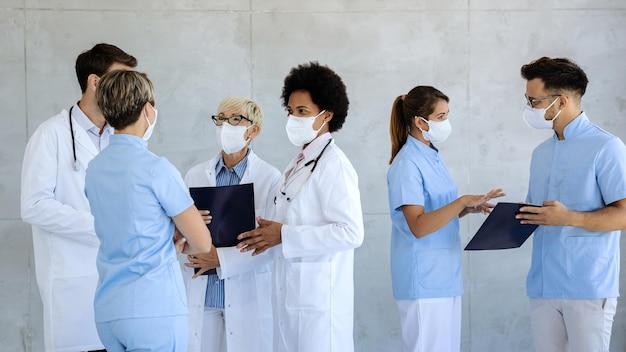 Gruppe von Mitarbeitern des Gesundheitswesens mit schützenden Gesichtsmasken, die auf dem Flur des Krankenhauses sprechen
