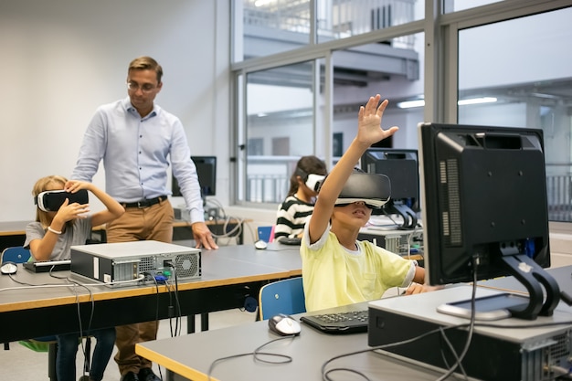 Gruppe von multiethnischen Kindern, die VR-Headsets tragen und Lehrer, die sie beobachten