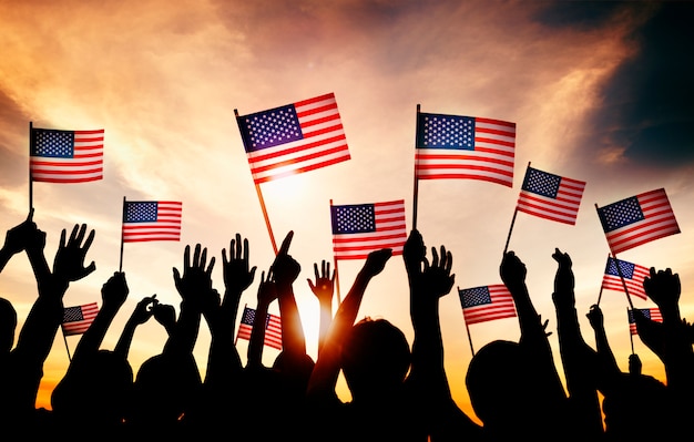 Gruppe von Personen, die amerikanische Flaggen in Gegenlicht wellenartig bewegt