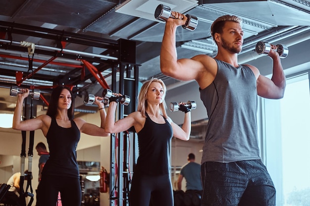 Gruppe von Personen, die im Fitnessclub oder im Fitnessstudio mit Hanteln trainieren.