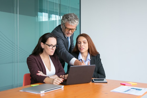 Gruppe von Top-Managern, die die Projektpräsentation auf einem Laptop beobachten und diskutieren, wobei die männliche Führungskraft auf das Display zeigt, während weibliche Manager Details erklären