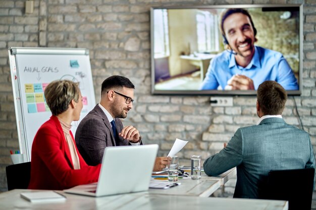 Gruppe von Unternehmern, die ein Geschäftstreffen abhalten und mit ihrem Kollegen per Videoanruf im Büro kommunizieren