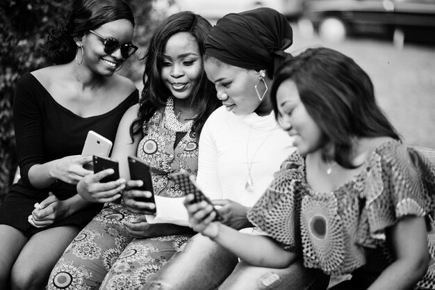 Gruppe von vier afroamerikanischen Mädchen, die auf einer Bank im Freien sitzen und Handys betrachten Schwarz und Weiß