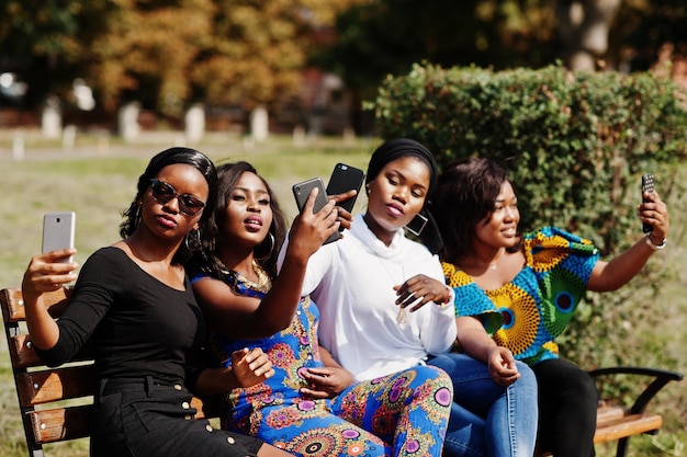 Gruppe von vier afroamerikanischen Mädchen, die mit Handys in der Hand auf einer Bank im Freien sitzen und Selfie machen