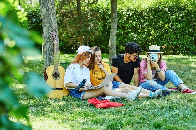 Gruppe von vier jungen Leuten, die Spaß im Park haben und auf dem Gras sitzen