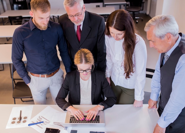 Kostenloses Foto gruppe wirtschaftler, die frau betrachten, die laptop am arbeitsplatz verwendet