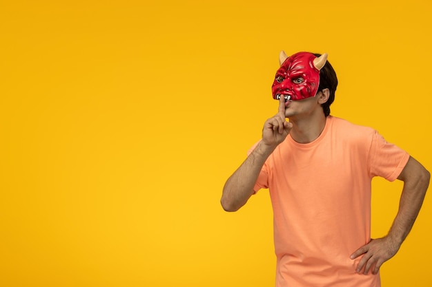 Gruselige Maske junger erschreckender Kerl, der Schweigezeichen in gruseliger roter Maske zeigt