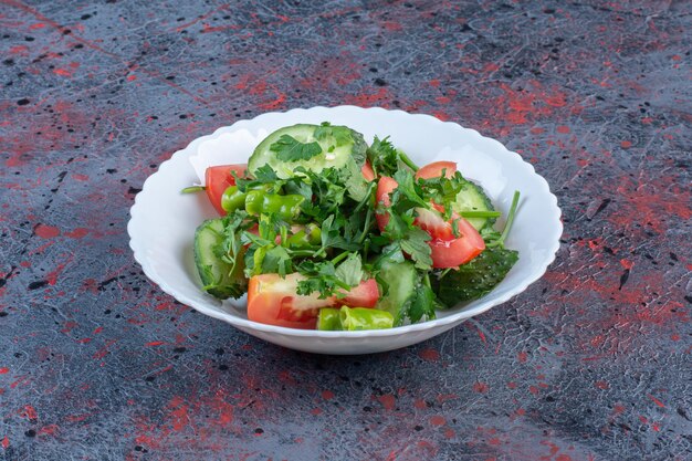 Gurken- und Tomatensalat gemischt mit Petersilienblättern auf dunklem Hintergrund. Foto in hoher Qualität