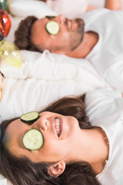 Gurkenscheiben über dem Gesicht des Paares auf dem Bett