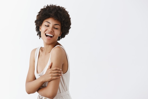 Gut aussehende emotionale und zarte weibliche Afroamerikanerin mit Afro-Frisur im trendigen Outfit, die sich umdreht und mit einem breiten Lächeln nach rechts schaut, Spaß und Freude empfindet