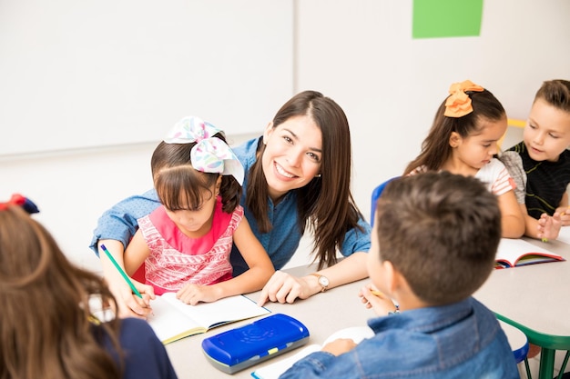 Gut aussehende hispanische Vorschullehrerin, die ihren Job genießt und Schüler in einem Klassenzimmer unterrichtet