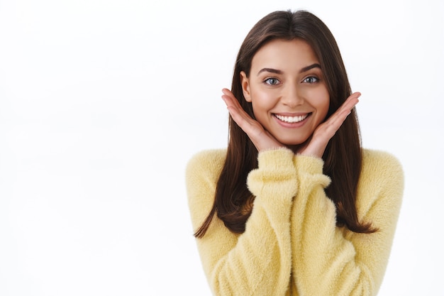 Gut aussehende weibliche brünette Frau mit perfektem strahlendem Lächeln und ohne Make-up-Haut, die ihr Gesicht berührt und zufrieden aussieht, ist Akne los geworden