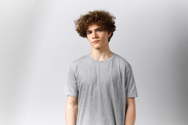 Gut aussehender junger europäischer Mann, der leeres graues T-Shirt mit Kopienraum für Ihre Schablone, Druck oder Design trägt und Kamera mit ernstem Ausdruck betrachtet