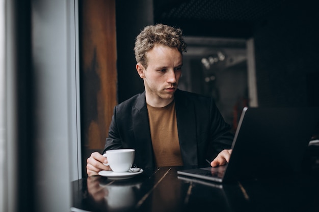 Gut aussehender Mann, der an einem Computer in einem Café arbeitet und Kaffee trinkt