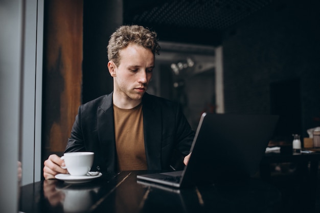 Gut aussehender Mann, der an einem Computer in einem Café arbeitet und Kaffee trinkt