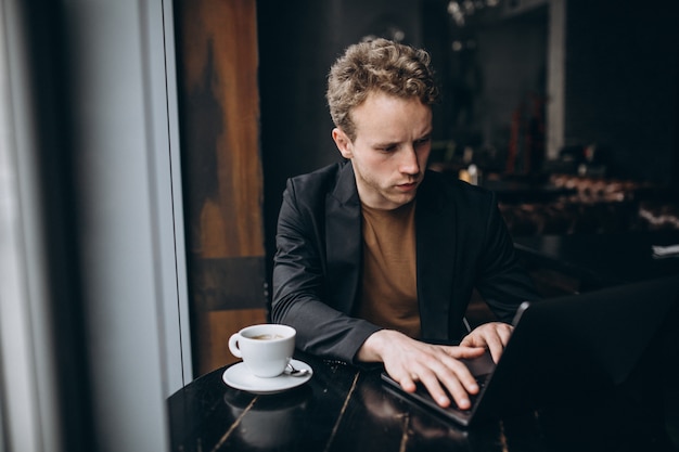 Gut aussehender Mann, der an einem Computer in einem Café arbeitet und Kaffee trinkt