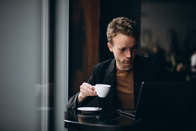 Gut aussehender Mann, der an einem Computer in einem Café arbeitet und Kaffee trinkt