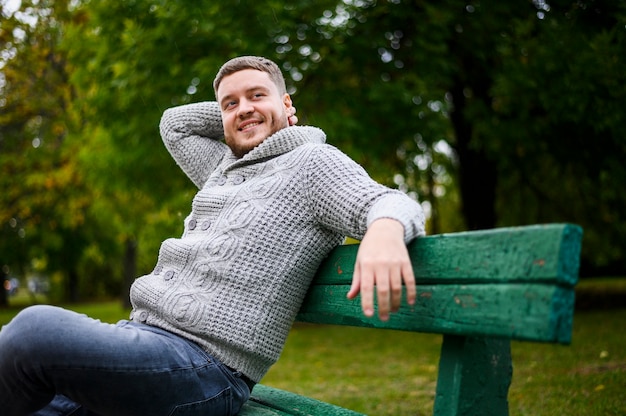 Kostenloses Foto gut aussehender mann, der auf einer bank im park lächelt