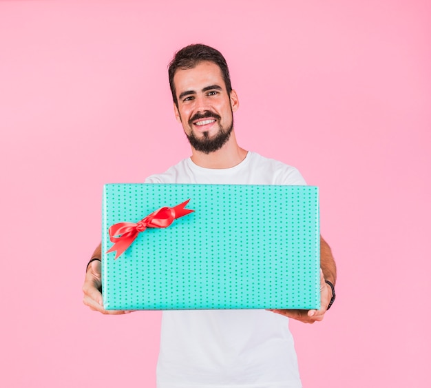 Gut aussehender Mann, der Geschenkbox gegen rosa Hintergrund hält