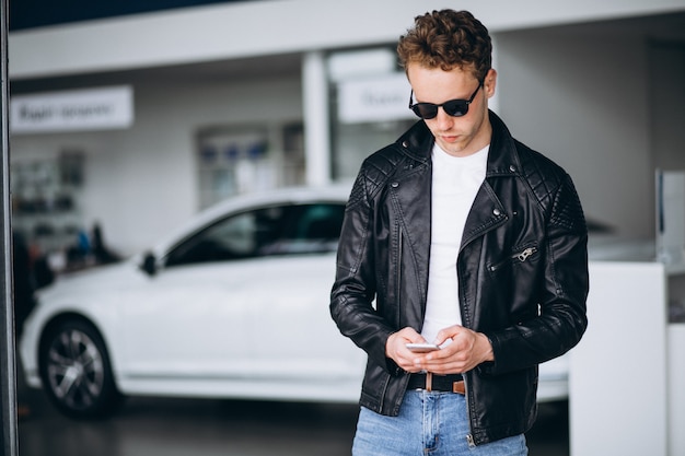 Gut aussehender mann, der telefon in einem autosalon verwendet