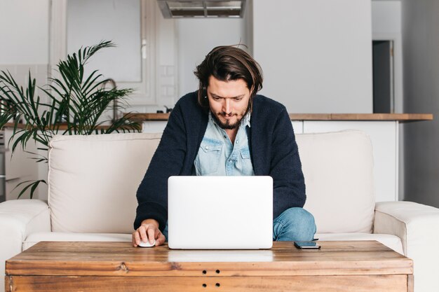 Gut aussehender Mann, der zu Hause auf Sofa unter Verwendung des Laptops sitzt