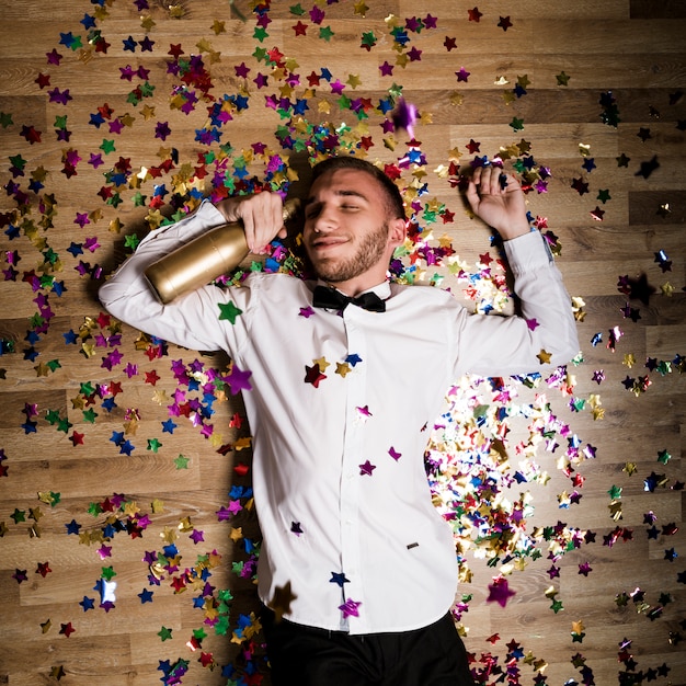 Kostenloses Foto gut aussehender mann im hemd mit flasche getränk zwischen konfetti