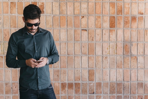 Gut aussehender Mann mit Smartphone nahe Backsteinmauer