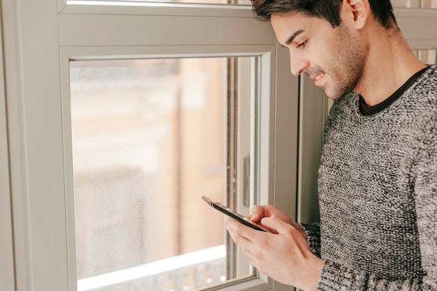 Kostenloses Foto gut aussehender mann mit smartphone nahe fenster