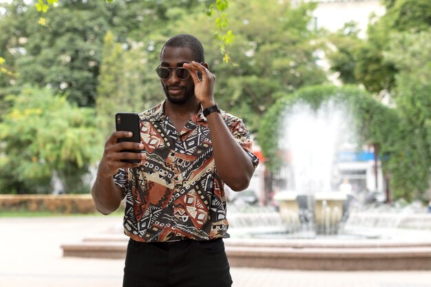 Gut aussehender Mann mit Sonnenbrille mit modernem Smartphone im Freien