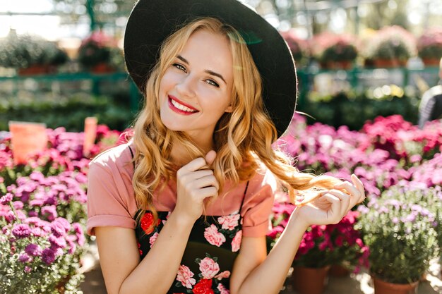 Gut gekleidete Frau, die im Frint der bunten Blumen aufwirft. Porträt einer glückseligen Frau, die mit ihren blinden Haaren spielt.