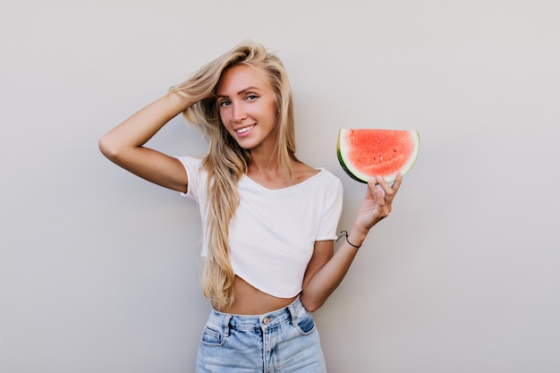 Gut gekleidete glückliche Frau, die Scheibe Wassermelone hält.
