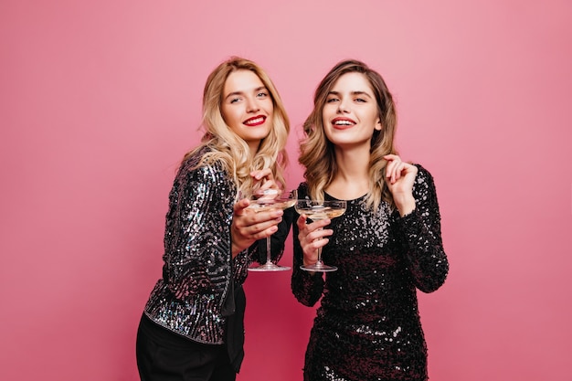 Gut gekleidetes Debonair-Mädchen, das Wein auf rosa Wand trinkt. Charmante kaukasische Damen, die sich auf der Party entspannen.
