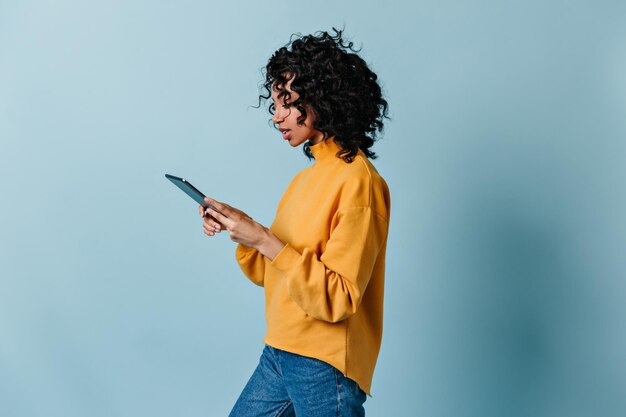Gut gekleidetes Mädchen mit digitalem Tablet Studioaufnahme einer hübschen jungen Dame im gelben Sweatshirt
