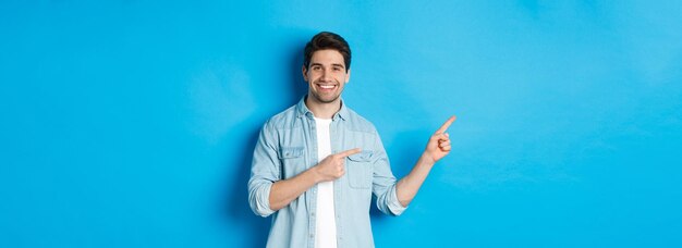 Gutaussehender kaukasischer Mann in lässigem Outfit, der mit dem Finger nach links zeigt und lächelnd Promo-Angebotsstandi zeigt