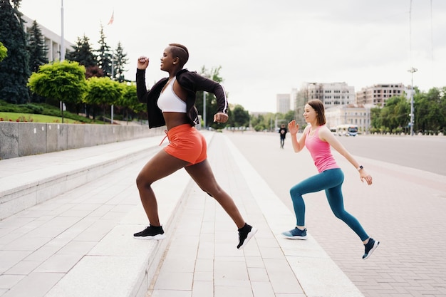 Gute Freunde in Sportbekleidung, die in der Stadt laufen, diskutieren über multiethnische Frauen, die ein Fitnesstraining machen