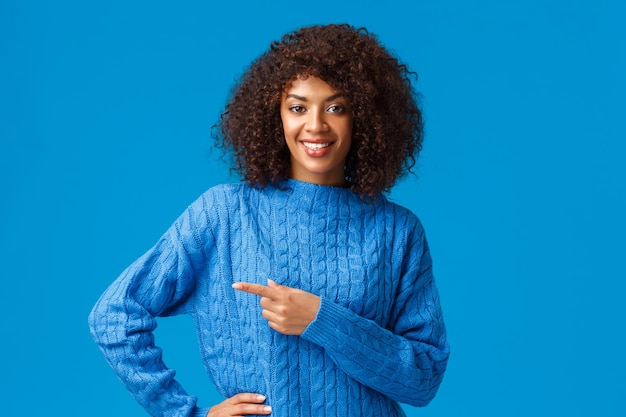 Guter Deal direkt über die Ecke. Selbstbewusste, angenehm freundlich aussehende afroamerikanische wunderschöne Frau mit Afro-Haarschnitt, die zur Kasse bittet, die Shop-Seite besucht, mit dem Finger nach links zeigt und eine lächelnde Kamera sucht.