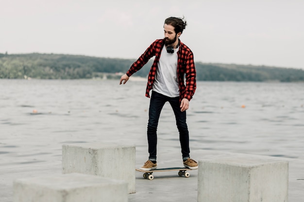 Guy in Flanell auf Skateboard an einem See