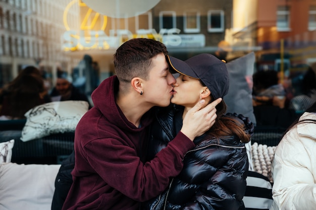 Guy und ein Mädchen küssen sich an einem Tisch in einem Straßencafé.