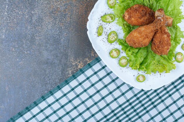 Hähnchenkeulen mit Pfeffer und Salat auf weißem Teller. Foto in hoher Qualität